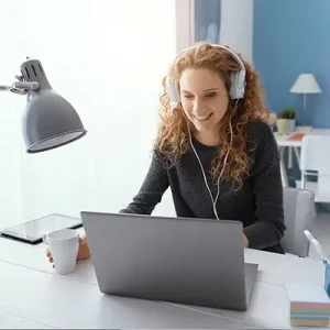 Ein Bild mit einer Frau mit Kopfhörern, die auf den Bildschirm eines zu ihr gerichteten Laptops schaut.